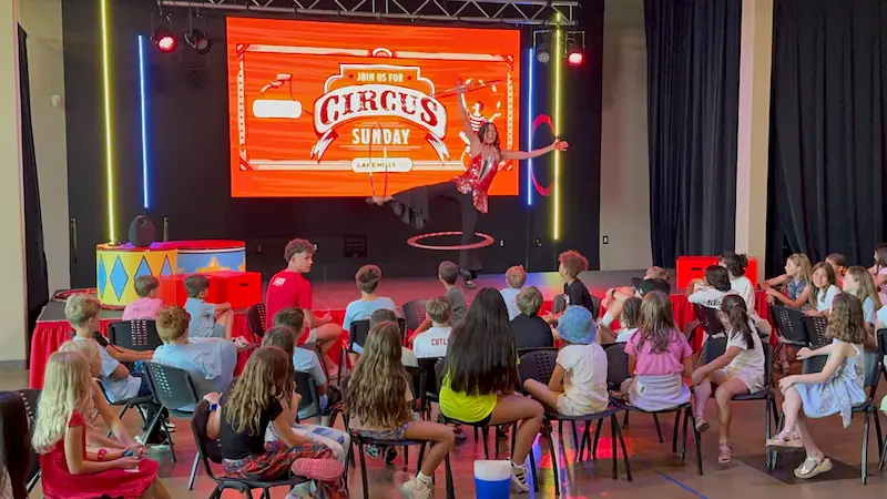 A hula hooper on stage performing for a large audience of kids